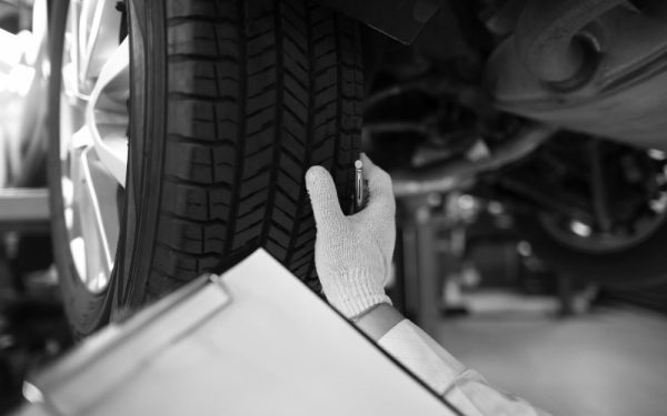 Close-up of mechanic writing on clipboard white examining car wheel. Inspector with tablet checking automobile before driving. Repair service station and maintenance concept